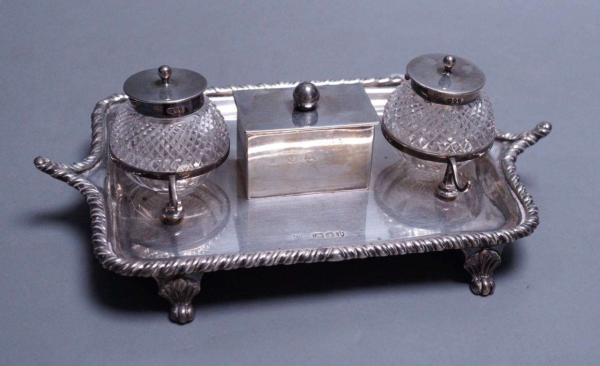 A late Victorian silver inkstand, with two mounted glass wells and central lidded compartment, Edward Hutton, London, 1890, 19cm, gross 9oz.